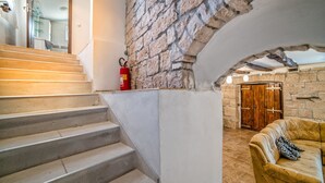 Una scala conduce a una stanza con un muro in pietra, una porta in legno e un divano in pelle con un cuscino decorato.