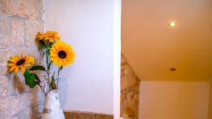 Un vaso bianco con girasoli su un davanzale piastrellato, sullo sfondo un muro in pietra.