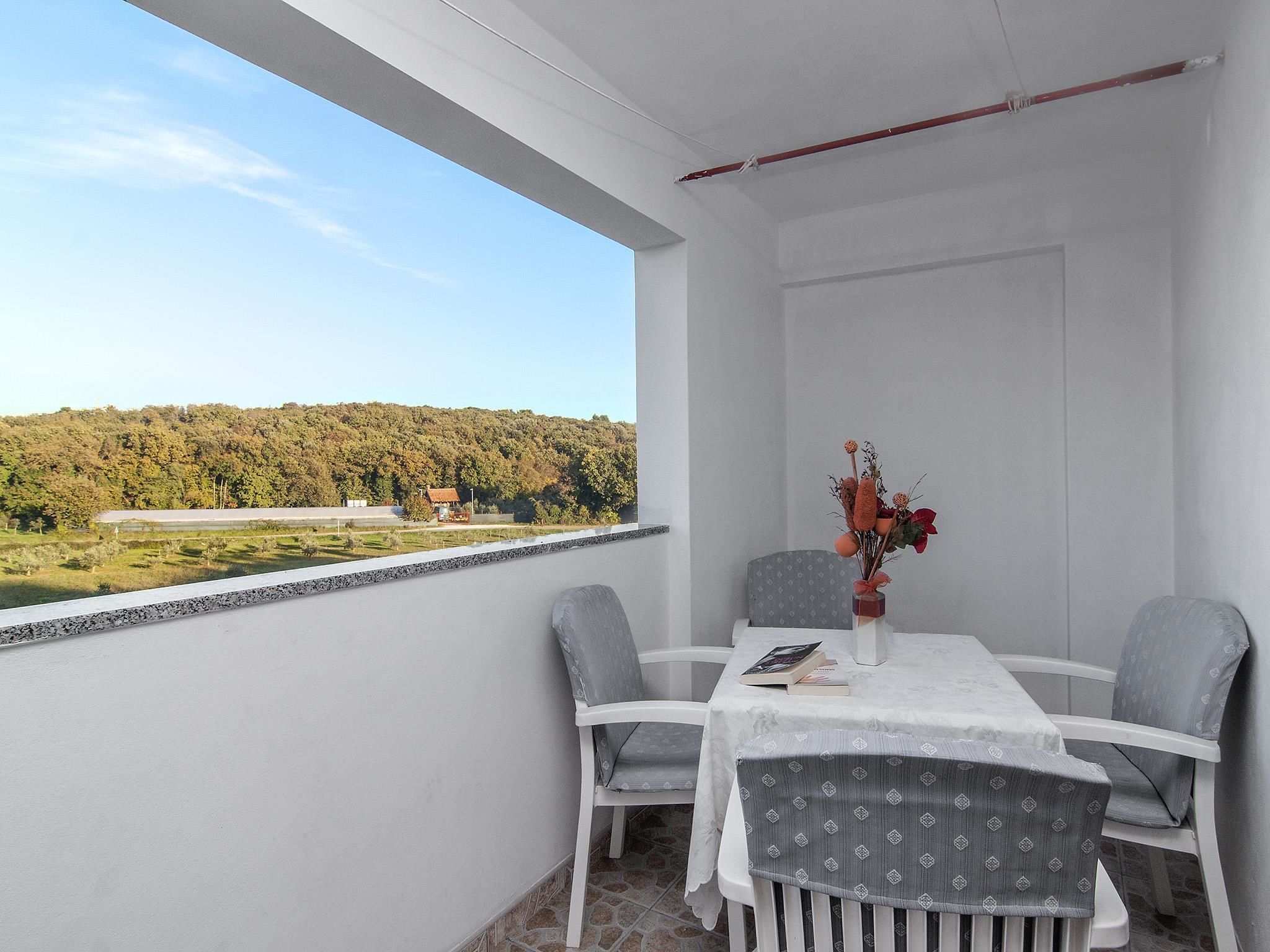 Een balkon met een tafel en stoelen, een bloemenvaas en uitzicht op een bebost gebied.