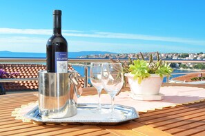 A bottle of wine, two glasses, and a potted plant on a table with a view of a coastal town. - Apartment Vesna Okrug Gornji / Two Bedroom A1 (Okrug)