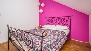 Une chambre à coucher avec un lit, un mur rose et un plancher en bois.