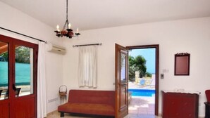 A room with a wooden sofa, a red cabinet, a chandelier, and a view of a swimming pool. - Villa Christodoula (Polis)