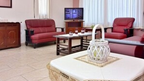 A living room with a red sofa, a coffee table with a decorative item, and a television on a wooden stand. - Villa Christodoula (Polis)