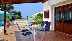 An outdoor patio with a table and chairs, a pool in the background, and a view of the sea. - Villa Christodoula (Polis)