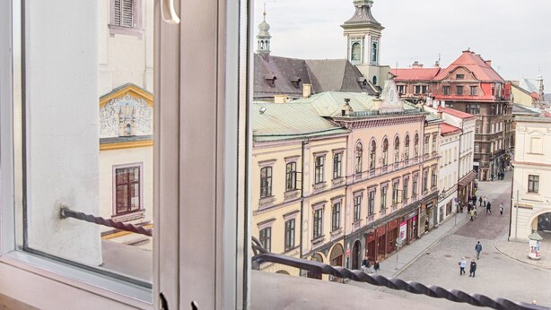 A window with a view of a city street, a clock, and a deer figurine. - Deer Apart (Cieszyn)