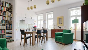 A modern living room with a green sofa, a dining table with chairs, a bookshelf, and a kitchen area in the background. - Deer Apart (Cieszyn)