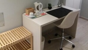 Un espacio de oficina moderno con un escritorio blanco, una silla, un televisor montado en la pared, un armario y un pequeño banco de madera.