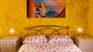 Una cama con ropa de cama floral, dos mesitas de noche y un cuadro en la pared de un pueblo costero.