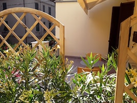 Una estructura de celosía de madera con plantas en primer plano, una pequeña mesa redonda y una silla al fondo.