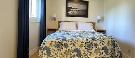 A bedroom with a bed, a window with curtains, a wall-mounted picture, and bedside lamps.