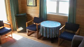 Ein gemütliches Zimmer mit Holzwänden, einem runden Tisch mit Blumenmuster-Tischdecke und vier blauen Stühlen.