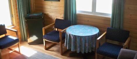 Ett mysigt rum med träväggar, ett runt bord med ett blommigt bordsduksöverdrag och fyra blå stolar.
