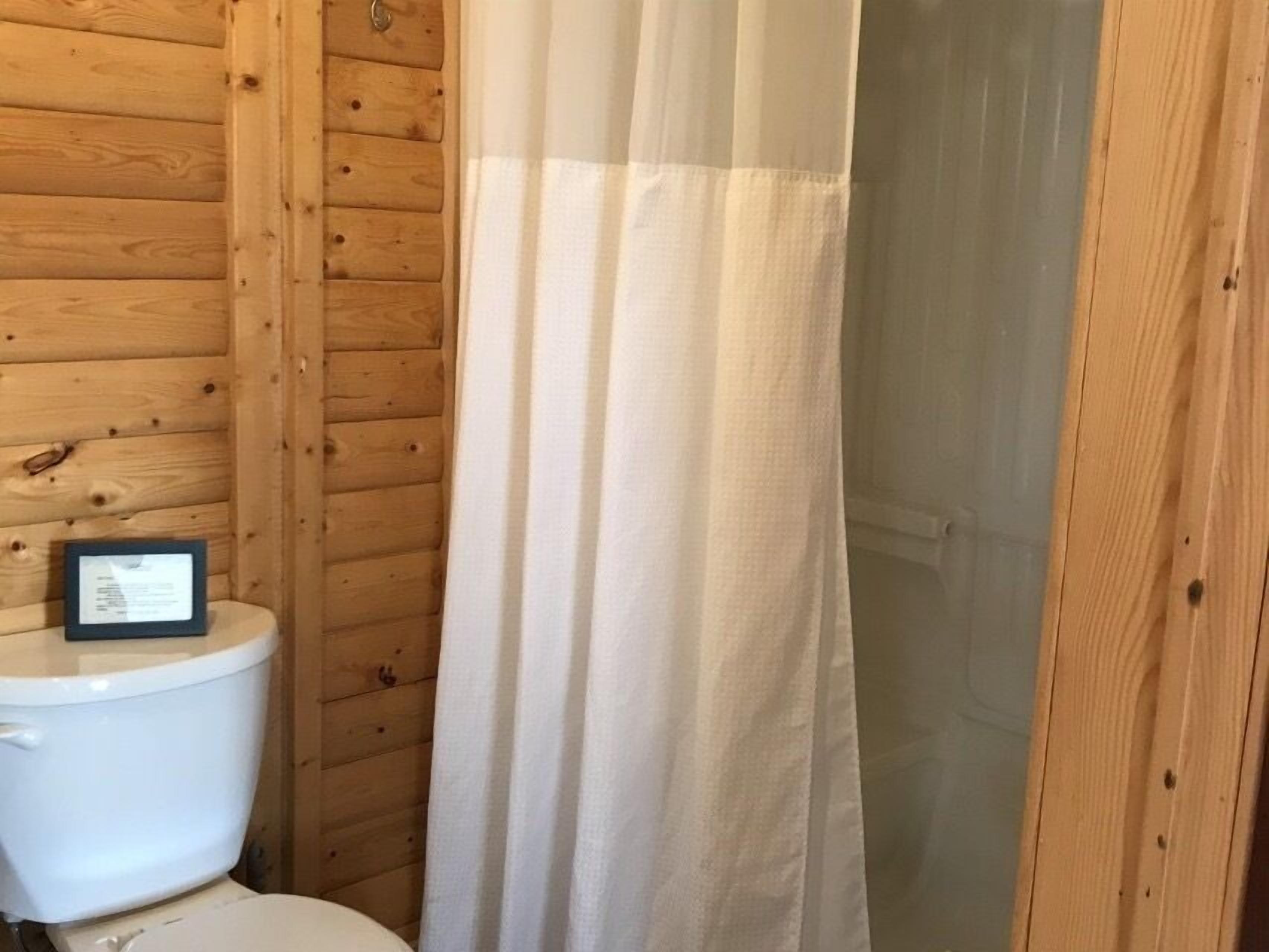 A wooden bathroom with a white toilet and a shower curtain.