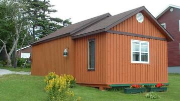 A wooden cabin with a pitched roof, a front door, and a small window.