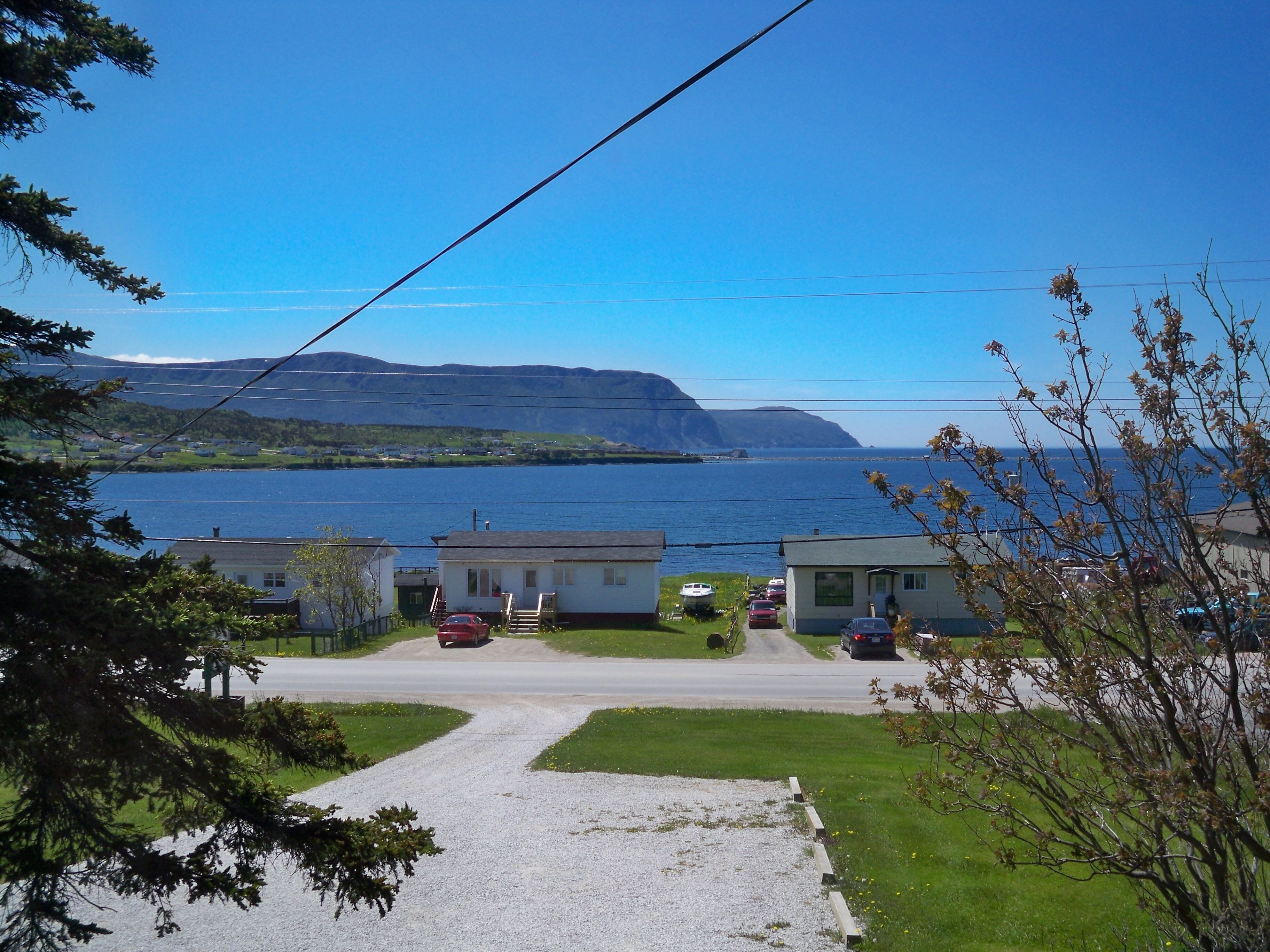 A coastal view with a gravel driveway leading to a row of houses, a body of water, and distant mountains.