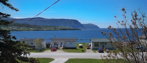 A coastal view with a gravel driveway leading to a row of houses, a body of water, and distant mountains.
