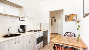 A compact kitchen with a sink, stove, and coffee maker. There is a wooden dining table with chairs and a vase with flowers. - Upper Apart (Cieszyn)