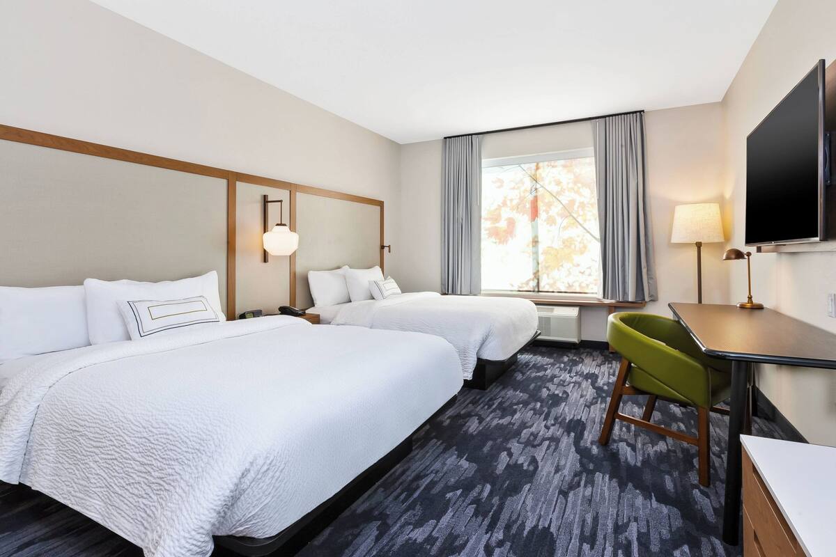 Habitación de hotel con dos camas, un escritorio, una silla, un televisor y una ventana con cortinas.