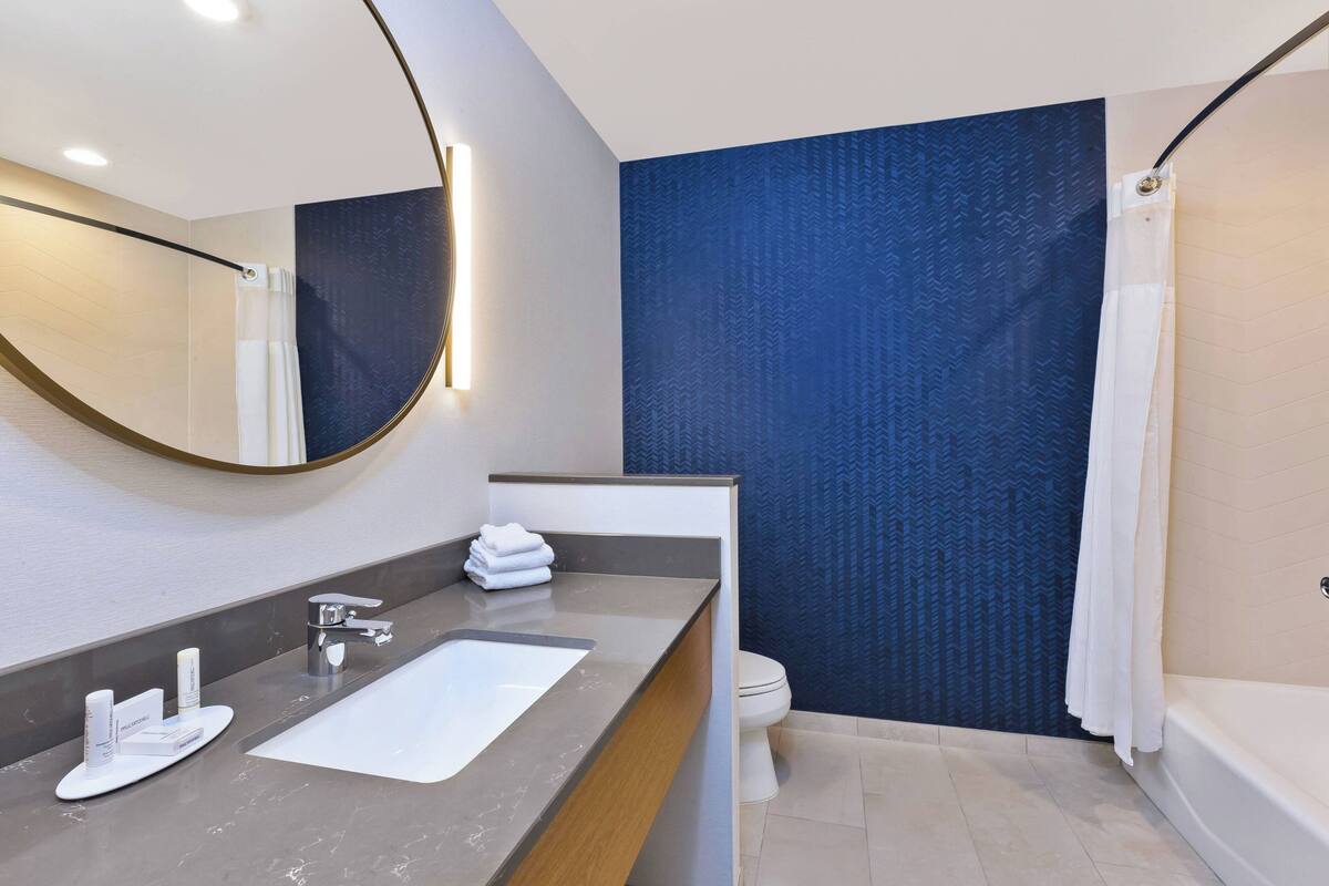 Un baño moderno con un espejo grande, un lavabo con artículos de aseo, un inodoro y una zona de ducha.