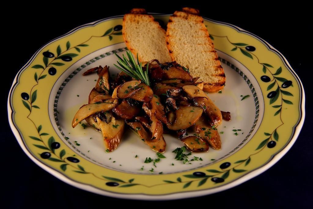 A plate of grilled mushrooms with a sprig of rosemary, served on a decorative yellow plate with a green olive pattern.