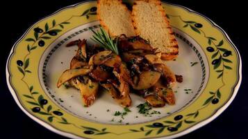 A plate of grilled mushrooms with a sprig of rosemary, served on a decorative yellow plate with a green olive pattern.