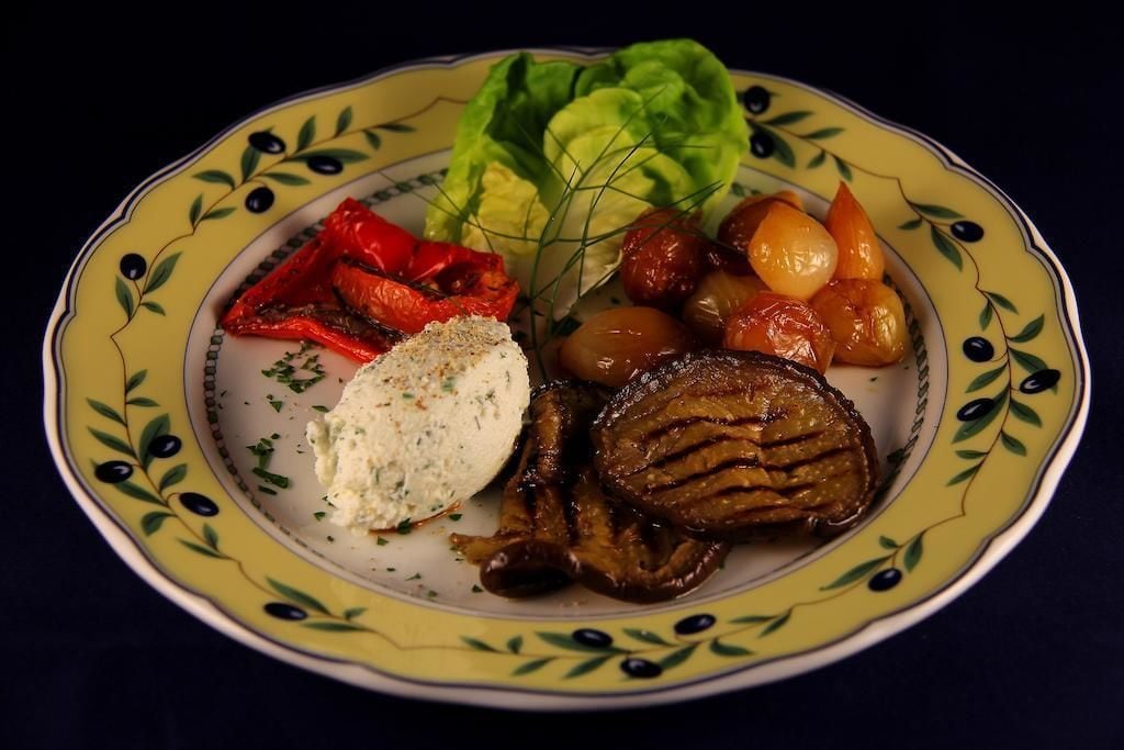 Une assiette garnie de viande grillée, de légumes rôtis et accompagnée d’une sauce.
