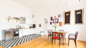 Uma cozinha moderna com armários brancos, piso xadrez preto e branco, e uma área de jantar com mesa e cadeiras de madeira.