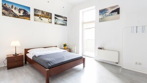 Quarto com cama de madeira, mesa de cabeceira, abajur, radiador e obras de arte nas paredes retratando paisagens.