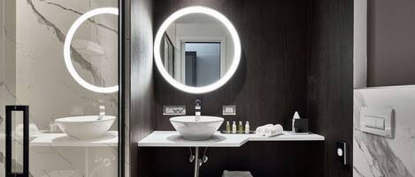Een moderne badkamer met een witte wastafel, een spiegel met ronde verlichting en een toilet.