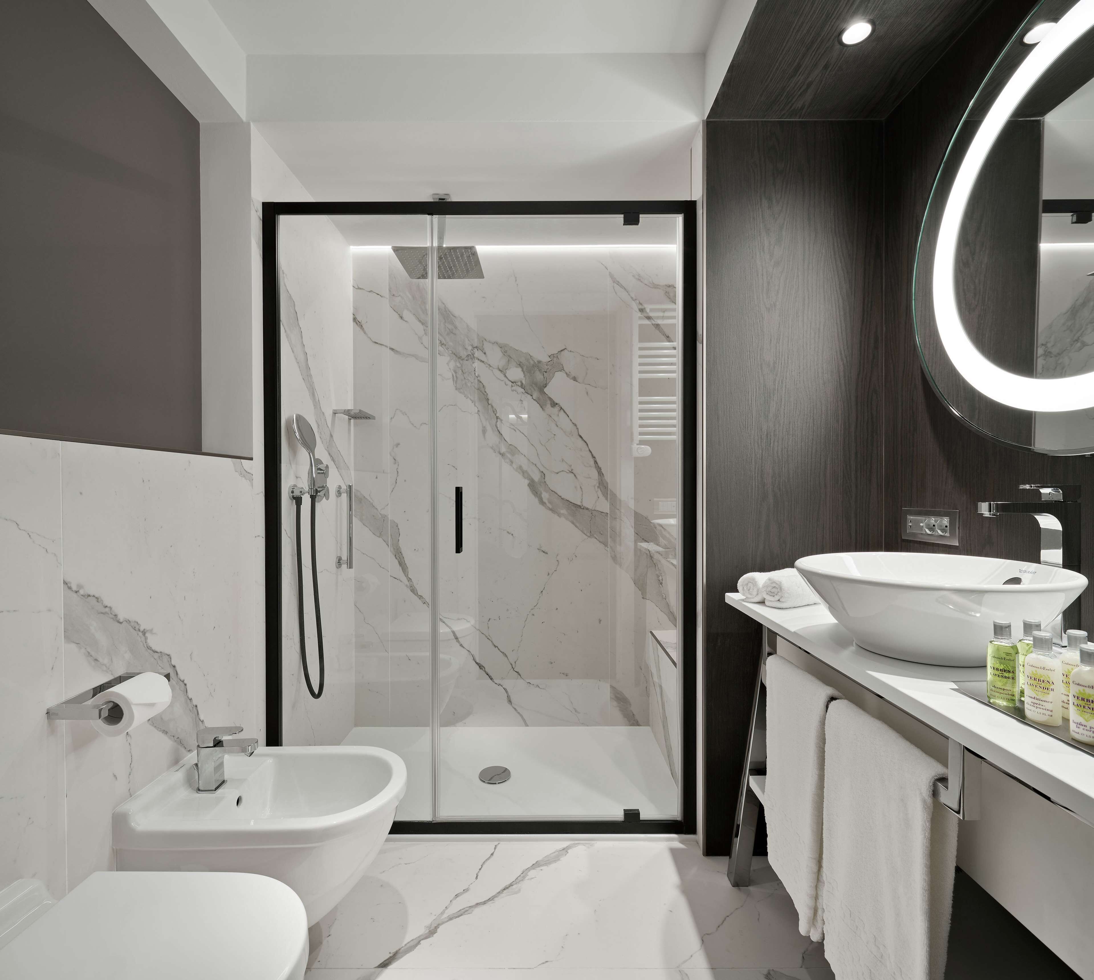 A modern bathroom with a glass-enclosed shower, a white sink, and a vanity with toiletries.