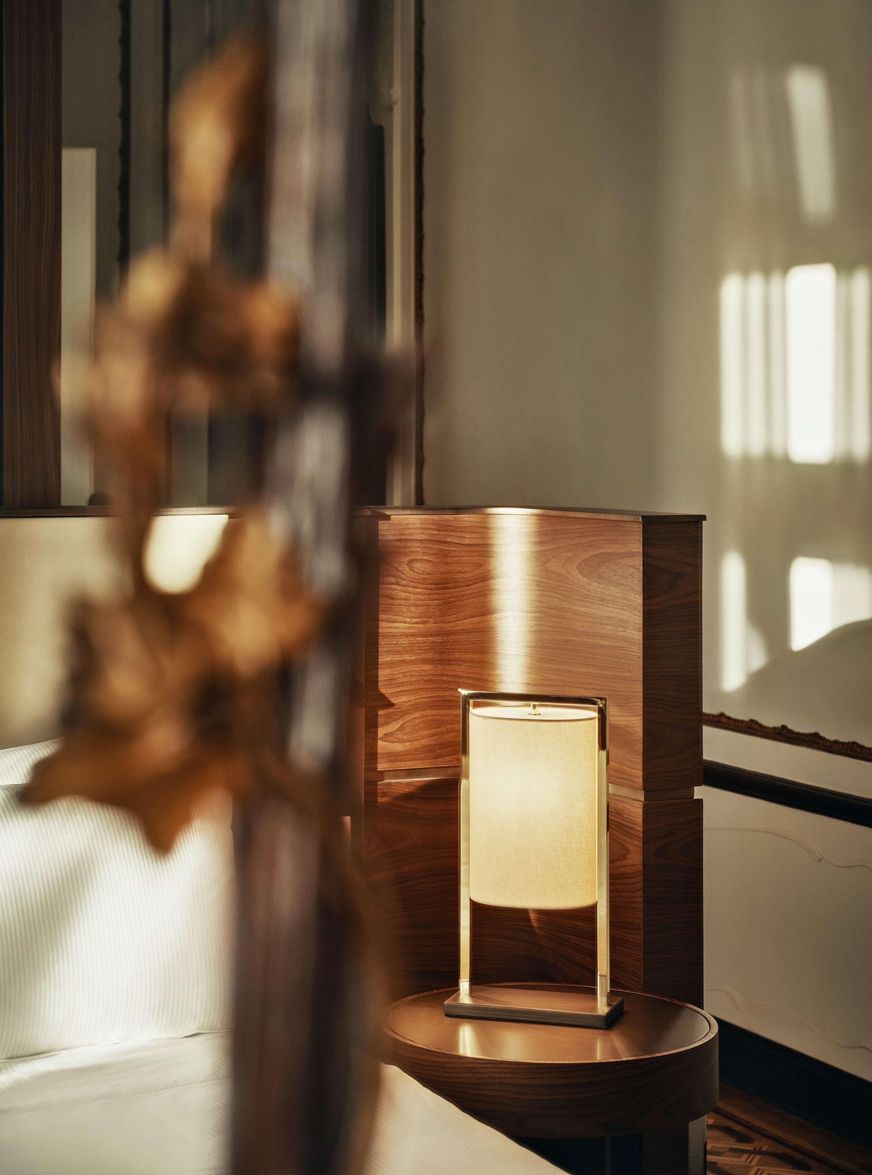 A modern room with a wooden side table holding a lit table lamp, a white sofa, and a decorative plant.