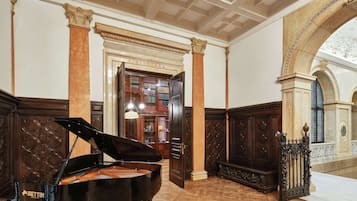 Un pianoforte a coda in un'ampia stanza con pannelli in legno decorati, una grande libreria e vista su un cortile attraverso un arco.