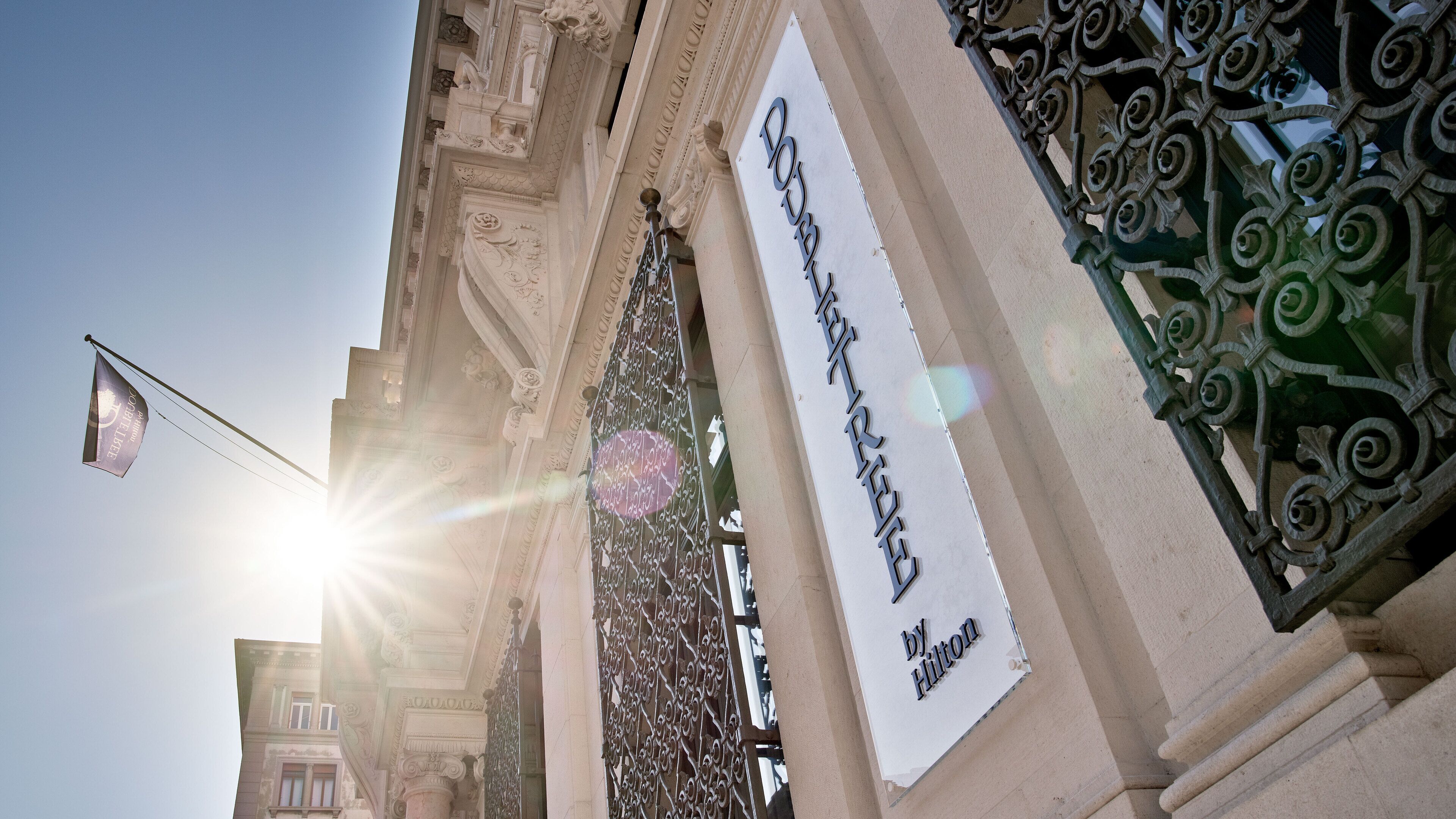 L’entrée d’un hôtel, avec une enseigne indiquant « by Hilton » et un portail en fer forgé à titre décoratif.