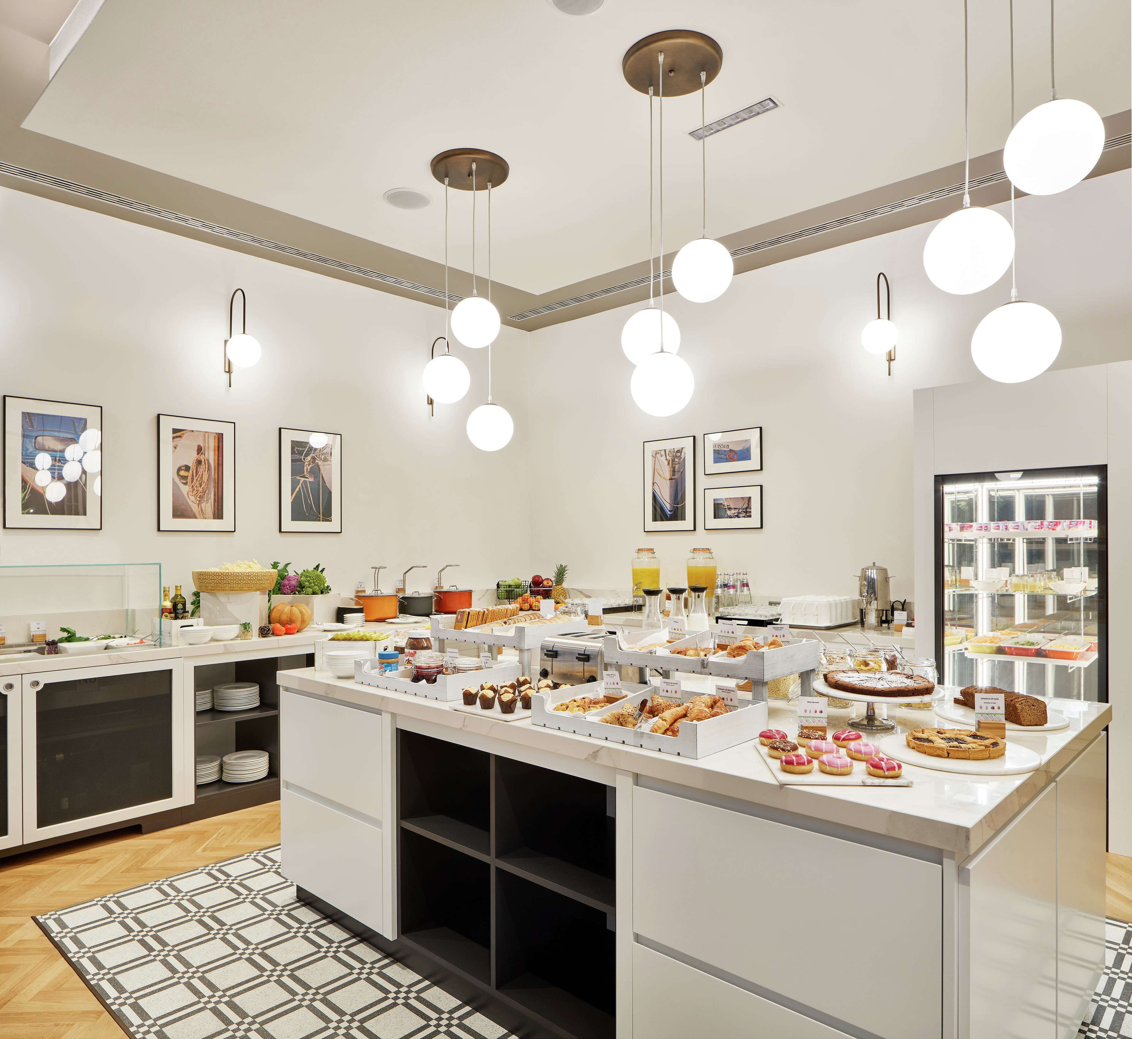A modern kitchen with a central island, pendant lighting, and various food items displayed.
