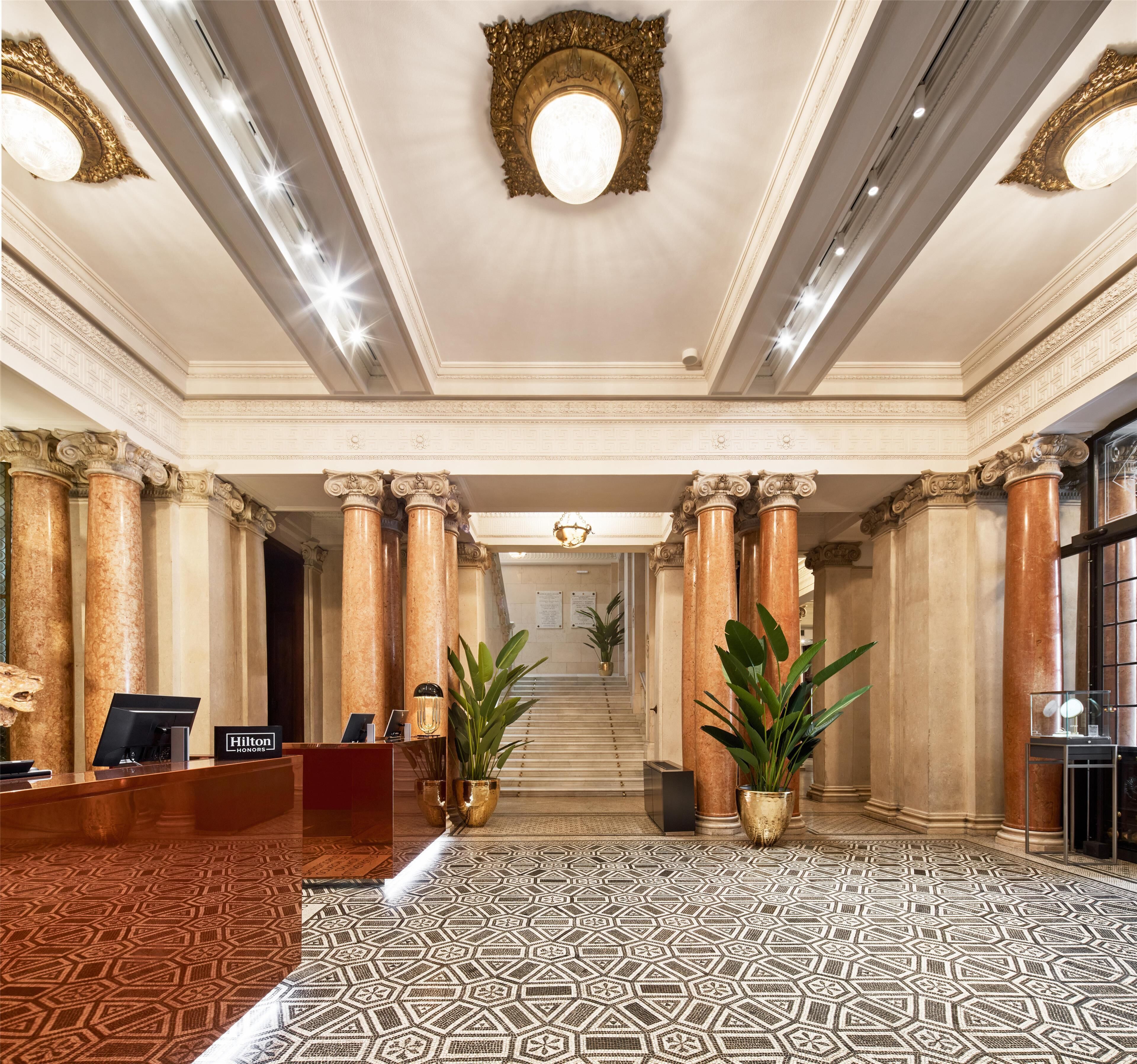 A grand lobby with marble columns, a reception desk, and a patterned floor.
