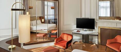 Quarto de hotel moderno com uma cama grande, uma escrivaninha, televisão e um espaço de estar com cadeiras laranja.