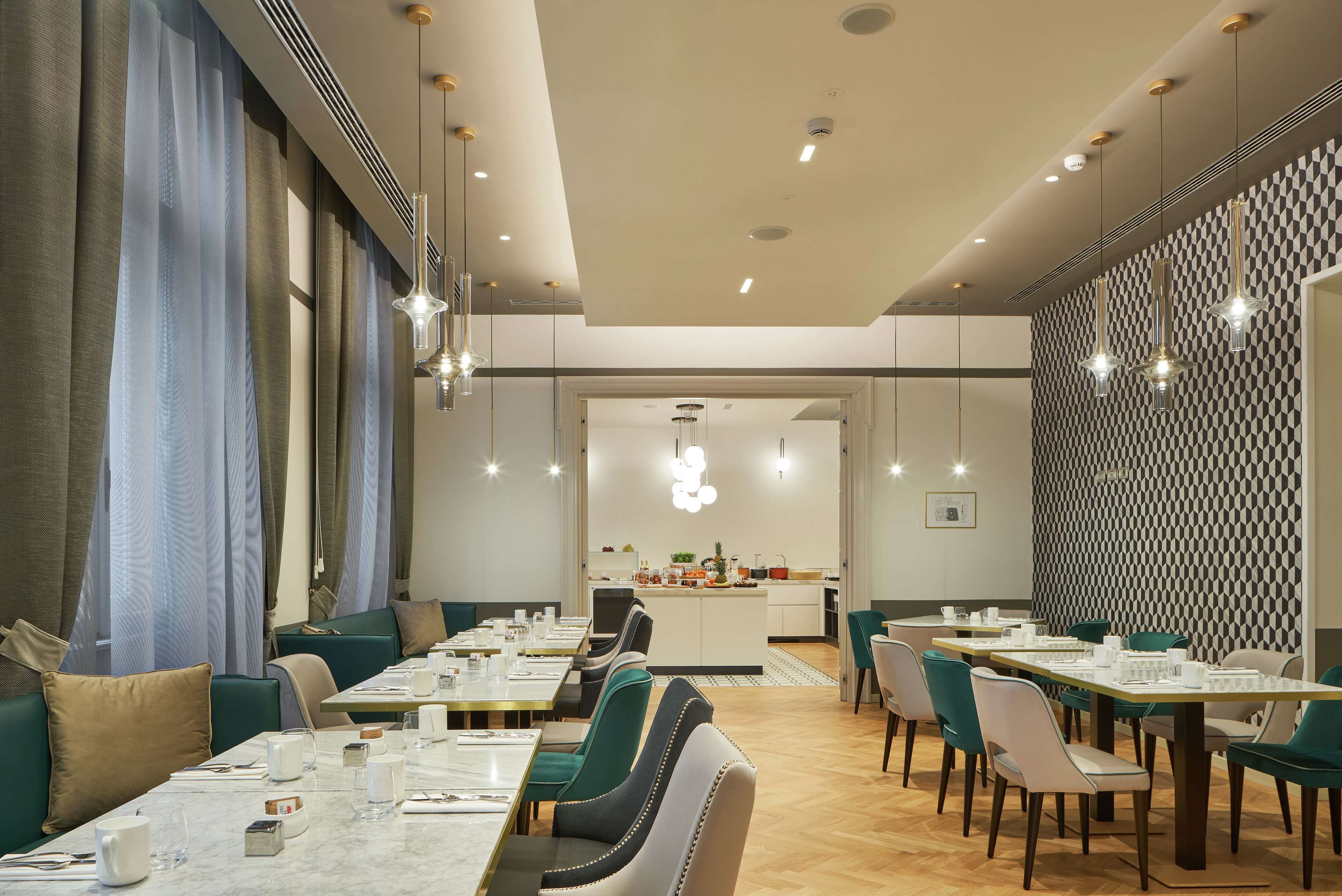 Un comedor moderno con mesas y sillas, una cocina al fondo y un muro con diseño.
