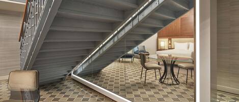 Una habitación de hotel moderna con una mesa de vidrio, un sofá y una escalera que conduce a otro nivel.