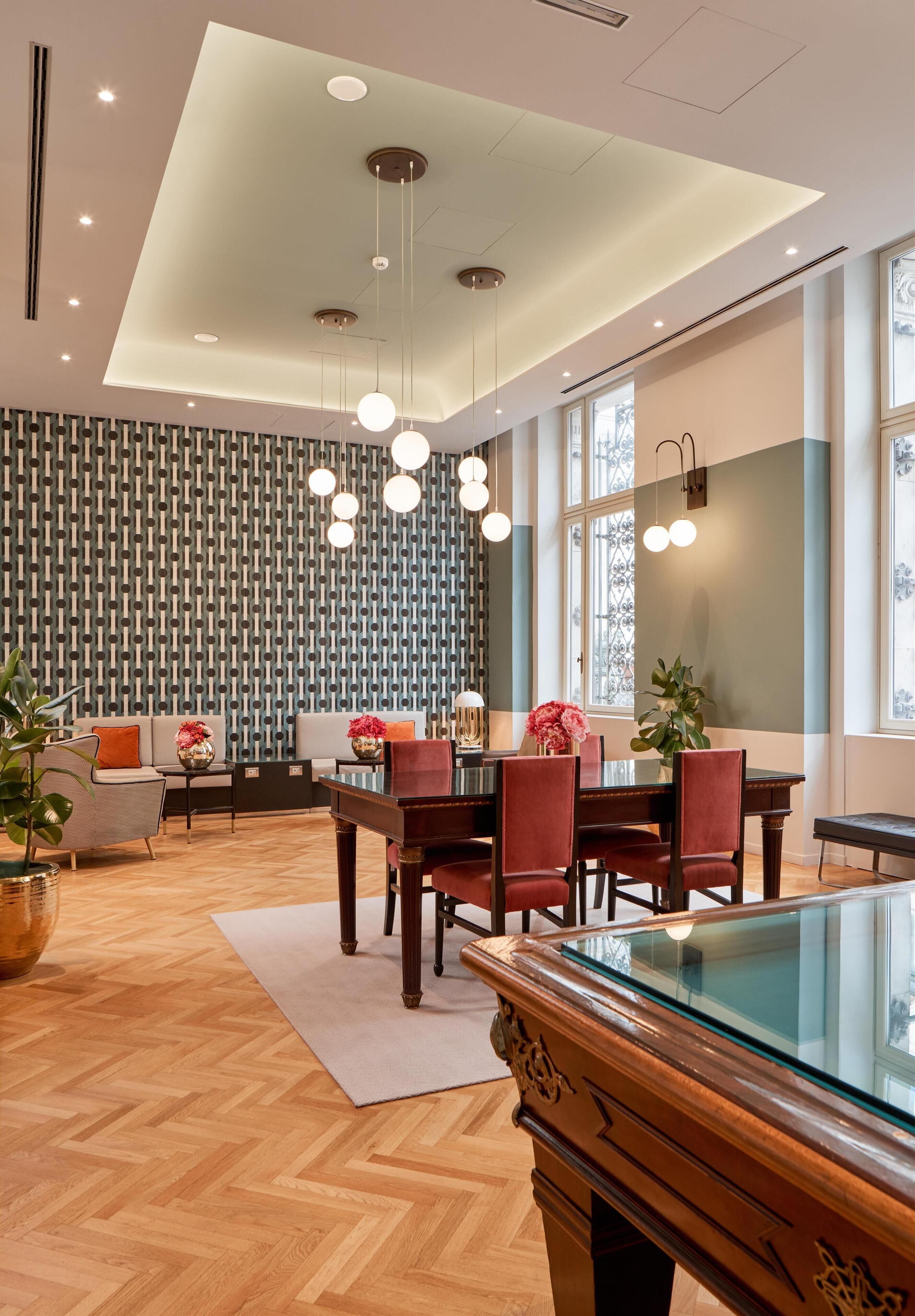 Un espace de salle à manger moderne avec un parquet en bois disposé en chevrons, une table à plateau en verre et des chaises à revêtement rouge.