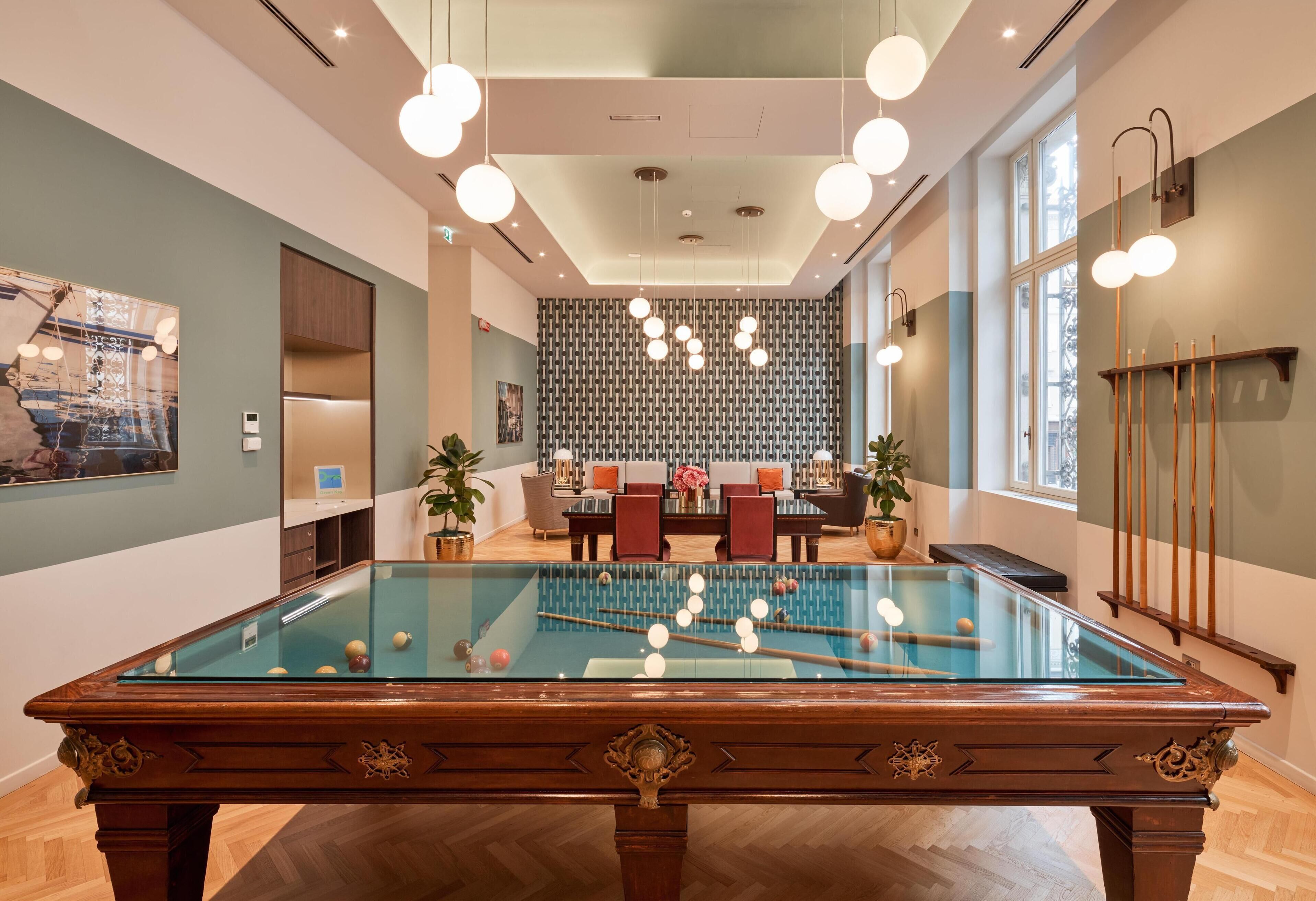 A pool table in a well-lit room with a modern design, featuring a patterned wall and a seating area with a table and chairs.