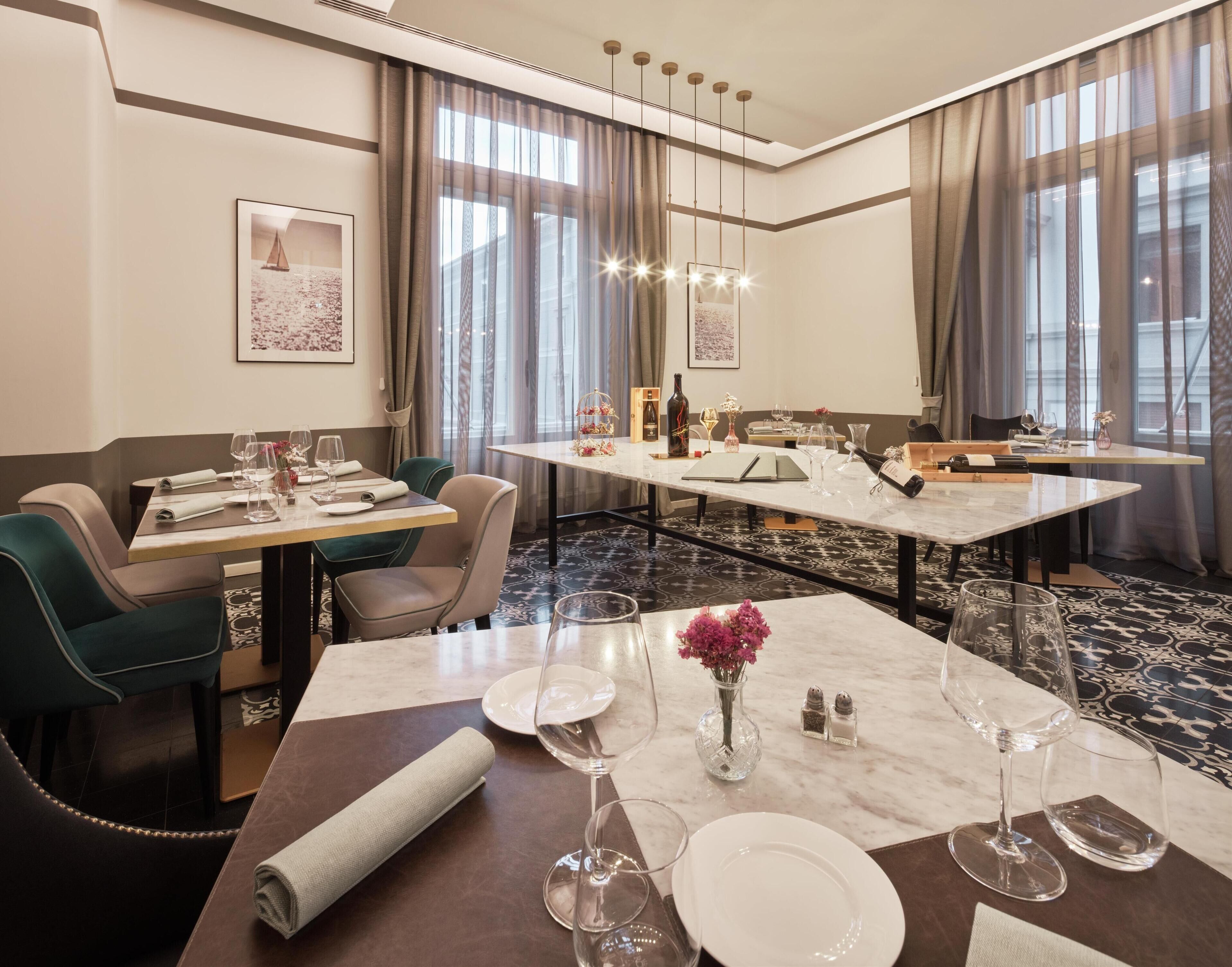Een restaurantgedeelte van een hotel met een lange tafel, stoelen en een kroonluchter.
