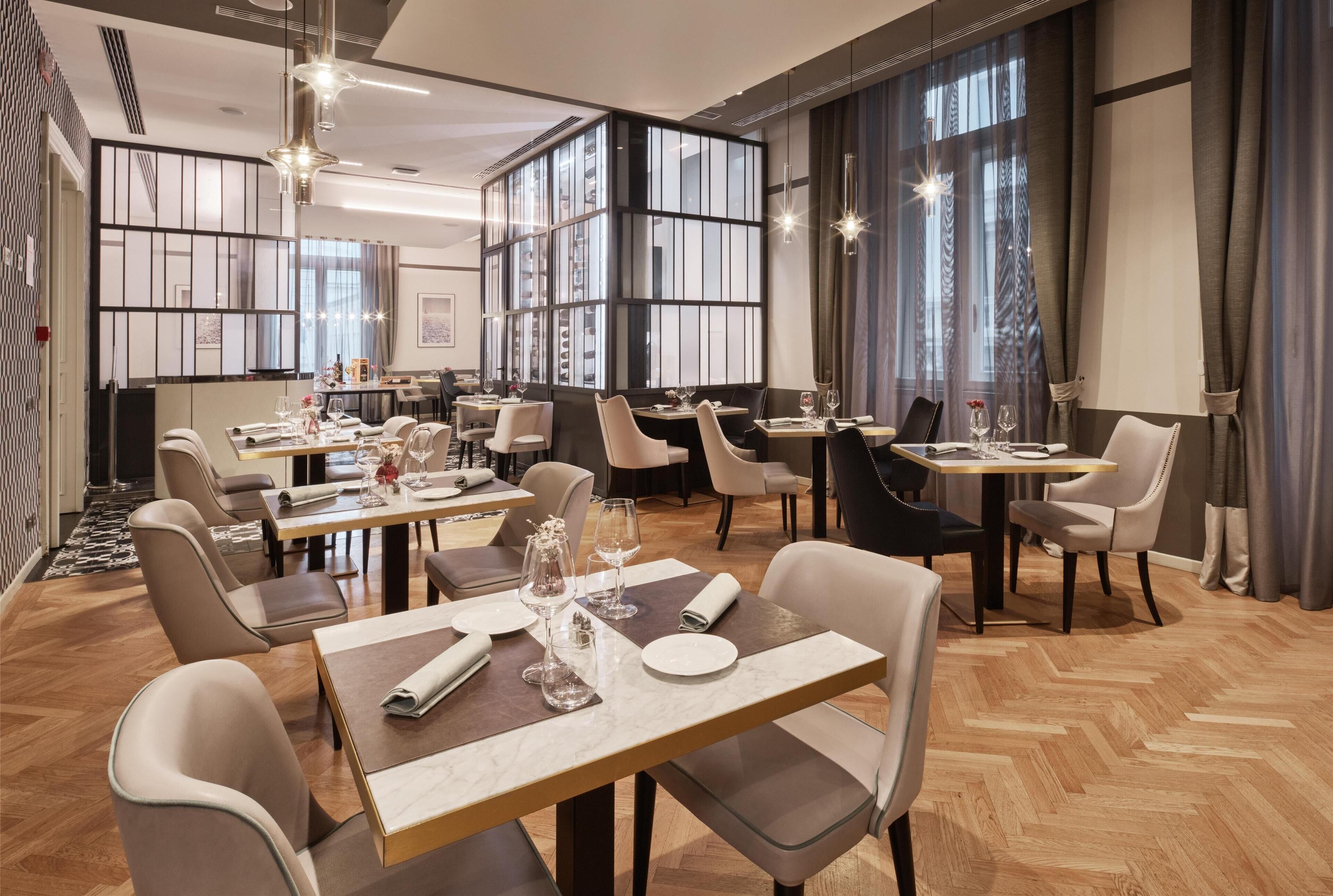 A modern dining area with multiple tables and chairs, large windows, and a decorative wall panel.