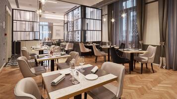 A modern dining area with multiple tables and chairs, large windows, and a decorative wall panel.
