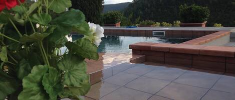 Et poolområde med udsigt til bjerge, omgivet af terrasserede beplantninger og krukker med planter.