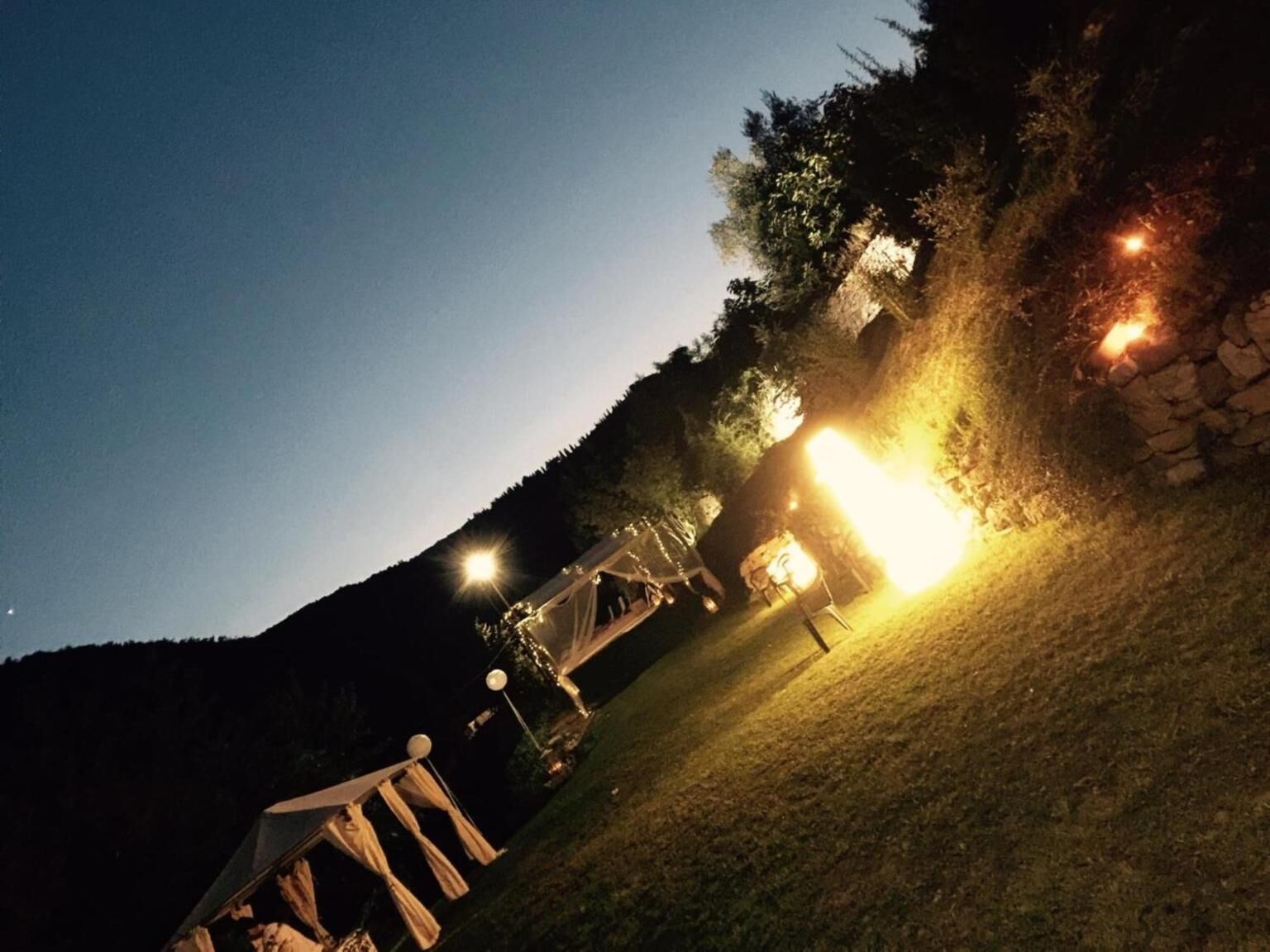 An outdoor event area with tents and a stone wall, illuminated by artificial lighting.