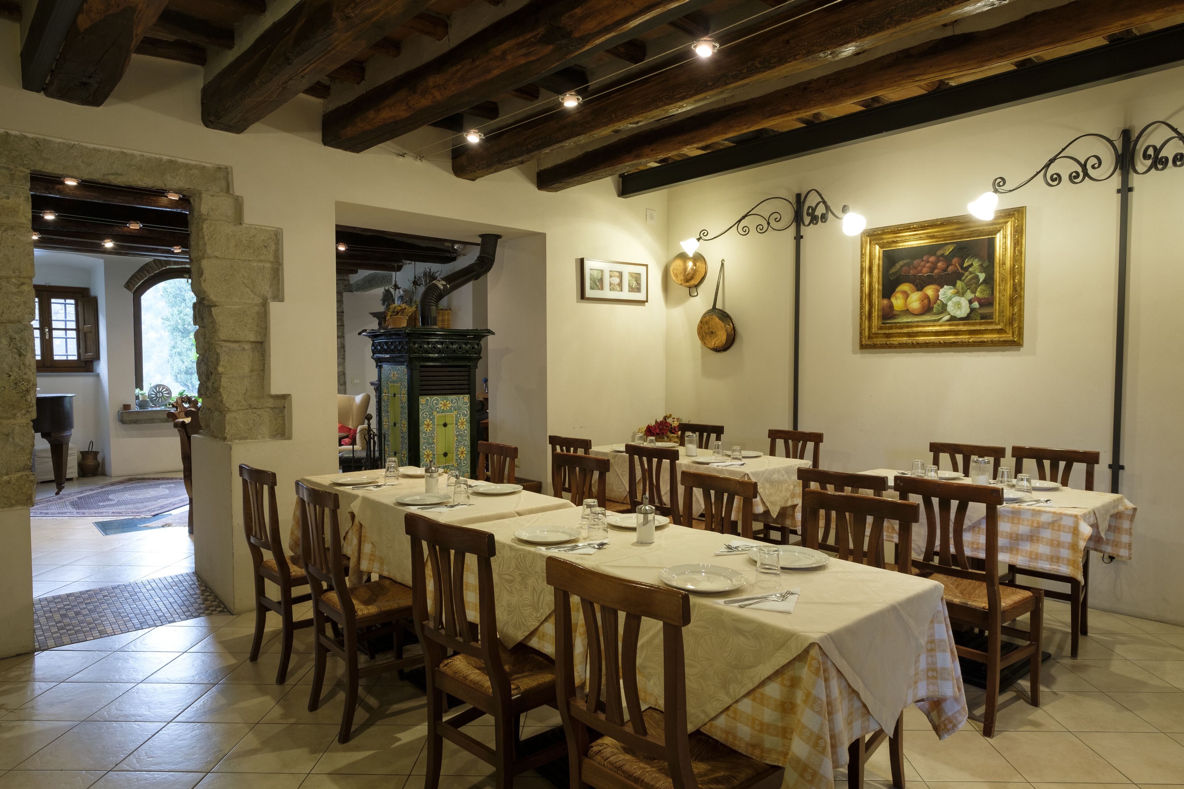 A dining area with multiple tables set for guests, wooden chairs, and a rustic ceiling with exposed beams.