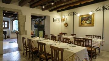 A dining area with multiple tables set for guests, wooden chairs, and a rustic ceiling with exposed beams.