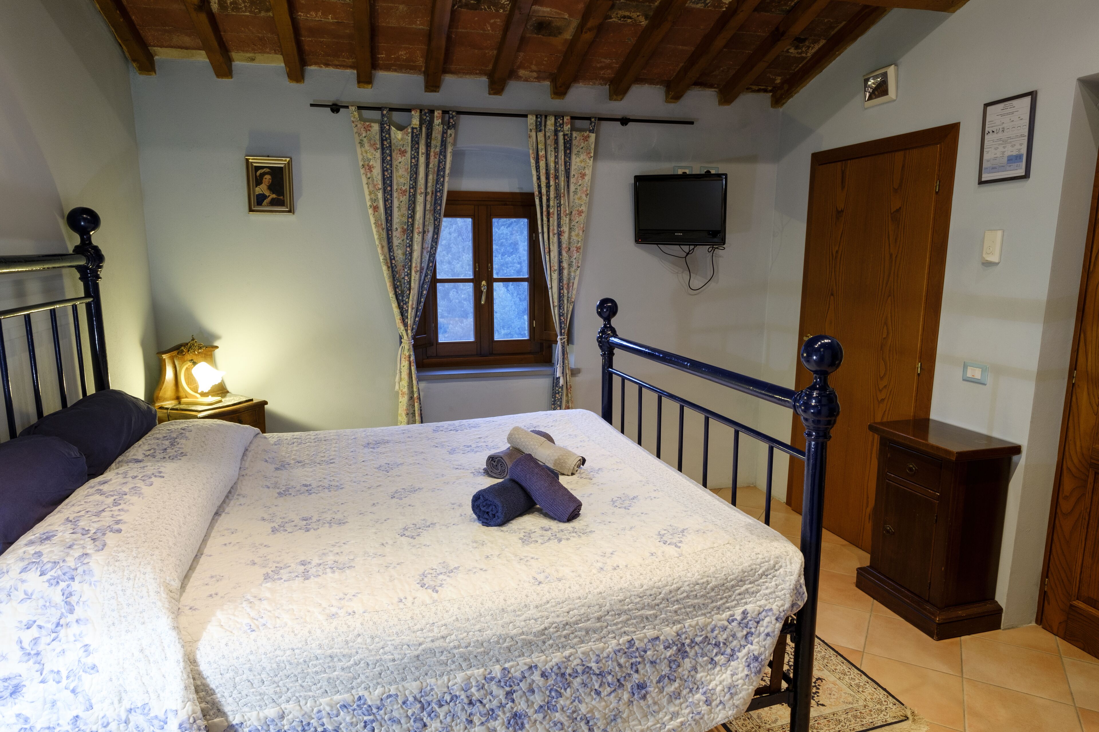 Une chambre à coucher comprenant un lit, une table de chevet, une armoire en bois, une fenêtre avec des rideaux et un téléviseur fixé au mur.