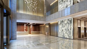 Um hall espaçoso com teto alto, uma recepção central e um design moderno com padrões geométricos nas paredes.