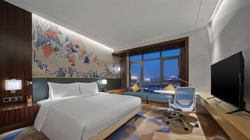 A hotel room with a large bed, a sofa, a TV, and a city view through the window.